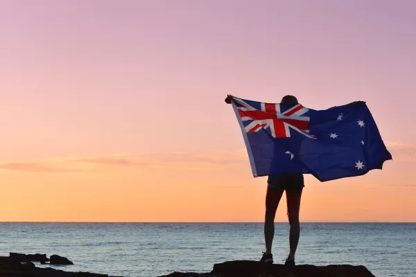 Someone holding an Australian flag at sunset on a clifftop